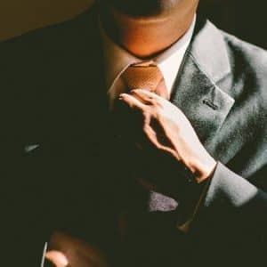 Homme en costume sombre ajustant sa cravate sous un éclairage contrasté et élégant.